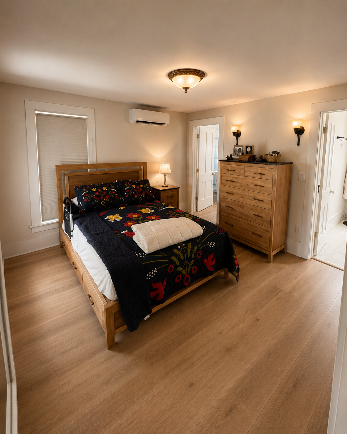 Renovated bedroom with light wood flooring, natural wood furniture, updated trim, and warm lighting.